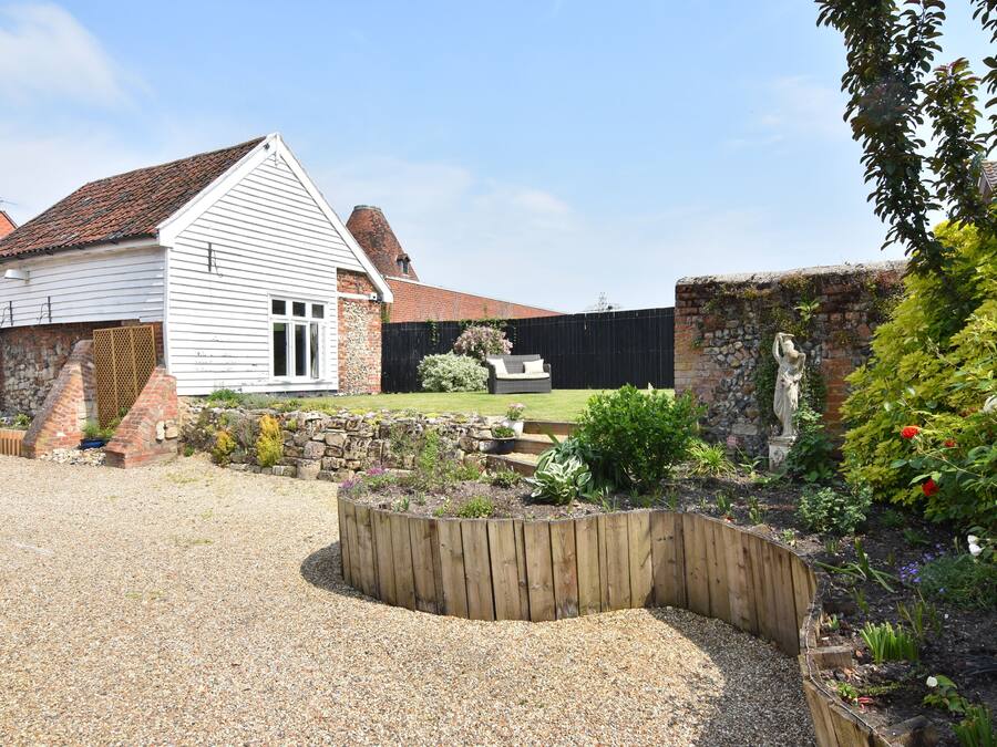 A white building with a red-tiled roof, surrounded by a garden with a wooden raised bed and a stone wall.