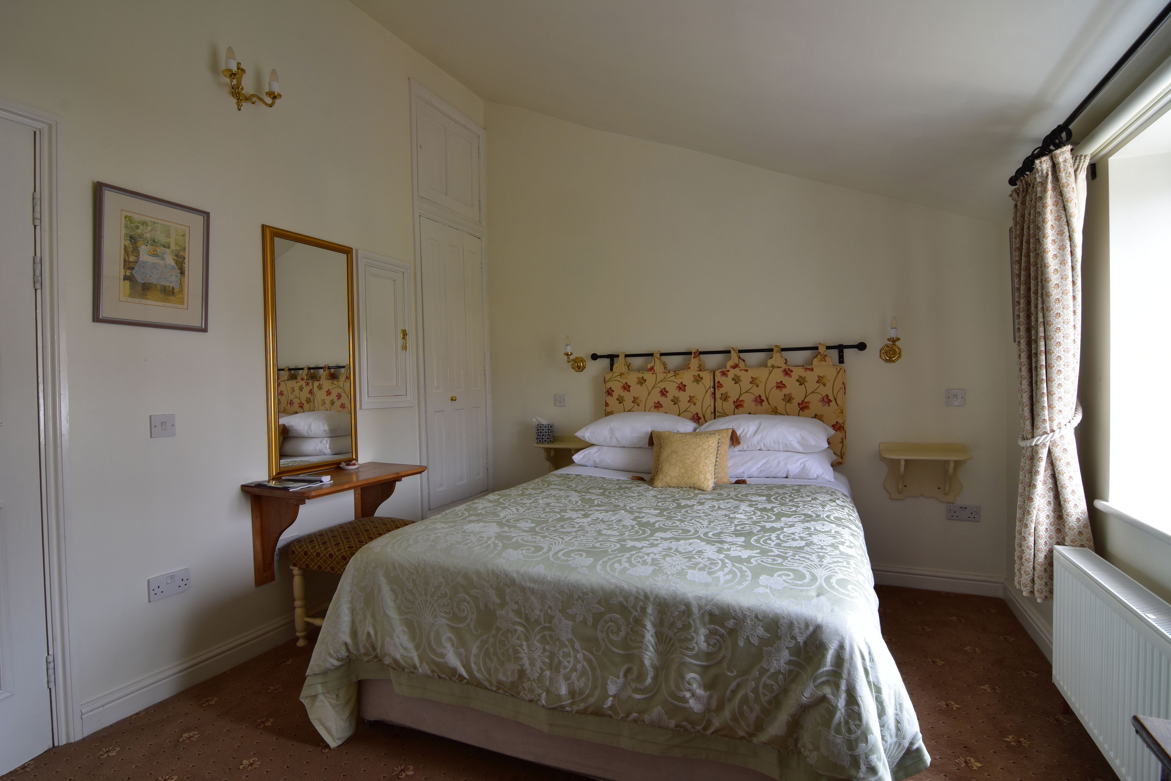 A bedroom with a bed, a dresser, a mirror, a bedside table, and a window with curtains.