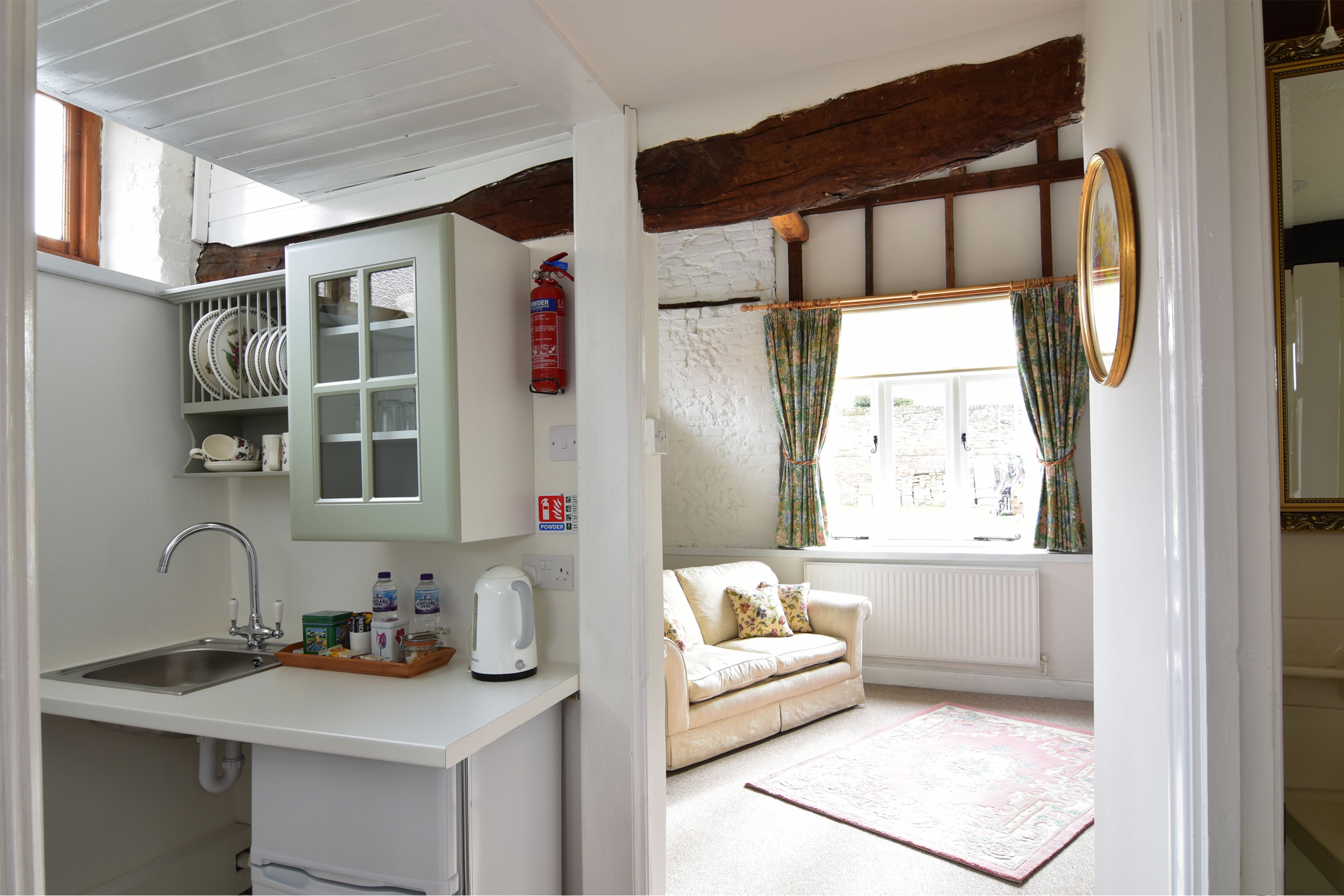 A compact kitchen with a sink, cabinets, and a window with curtains.