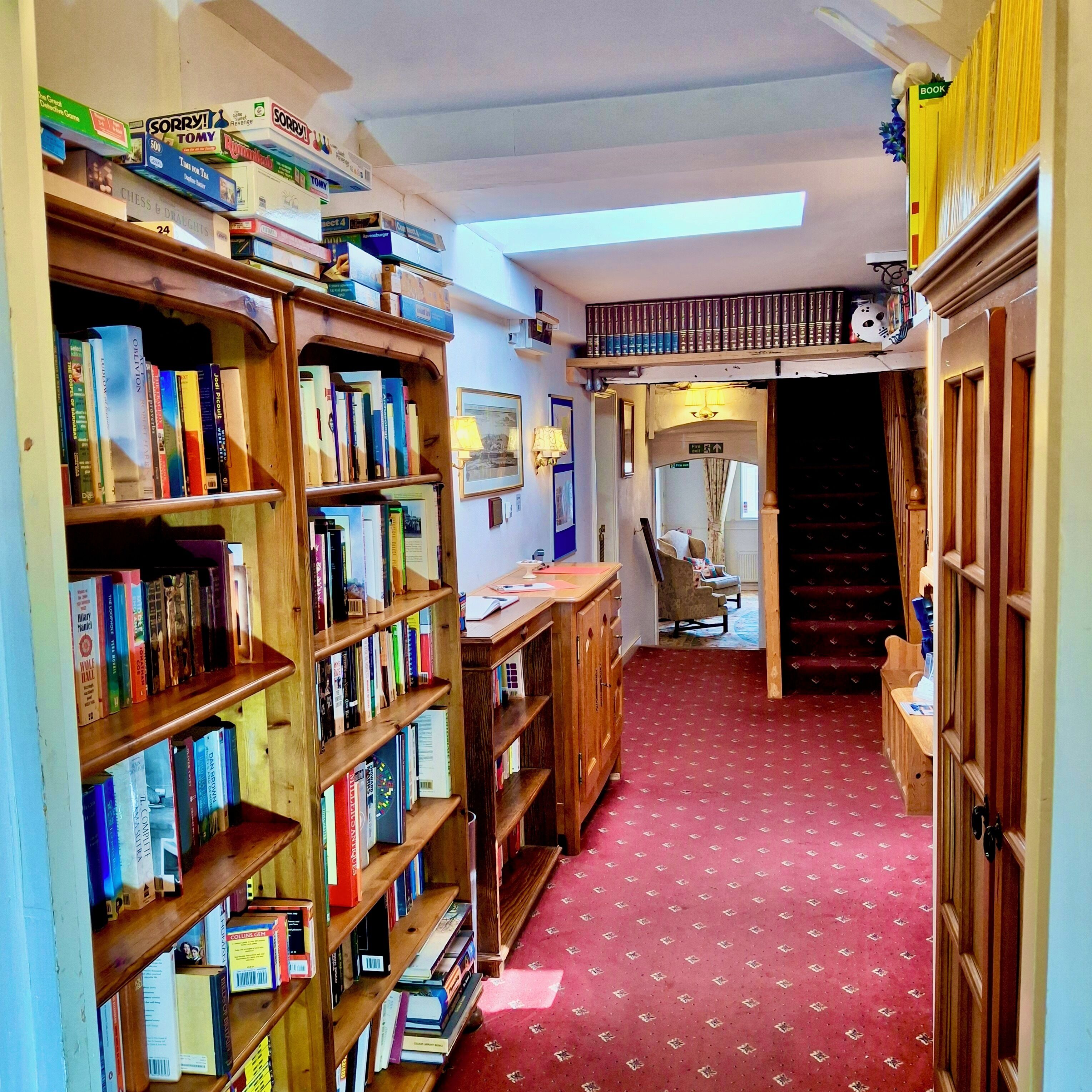 Un pasillo estrecho con estanterías de madera llenas de libros, una alfombra roja con estampado y una escalera que sube a un nivel superior.