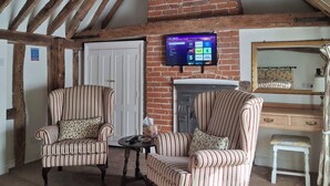 A room with a sloped ceiling, exposed wooden beams, a brick fireplace, and a mounted flat-screen TV displaying a streaming service interface.