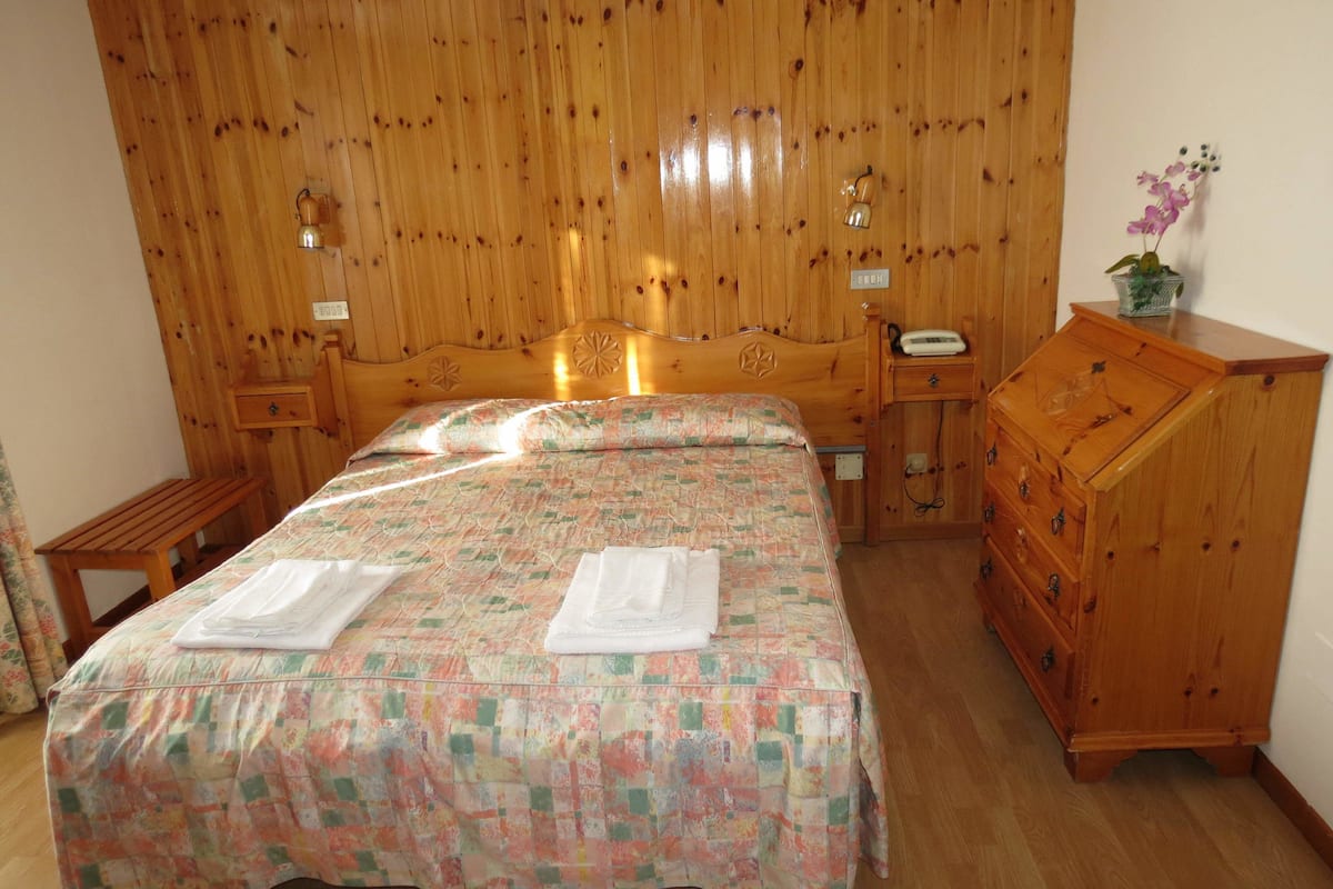Une chambre à coucher aux murs lambrissés, avec un lit, une commode en bois et une table de chevet.