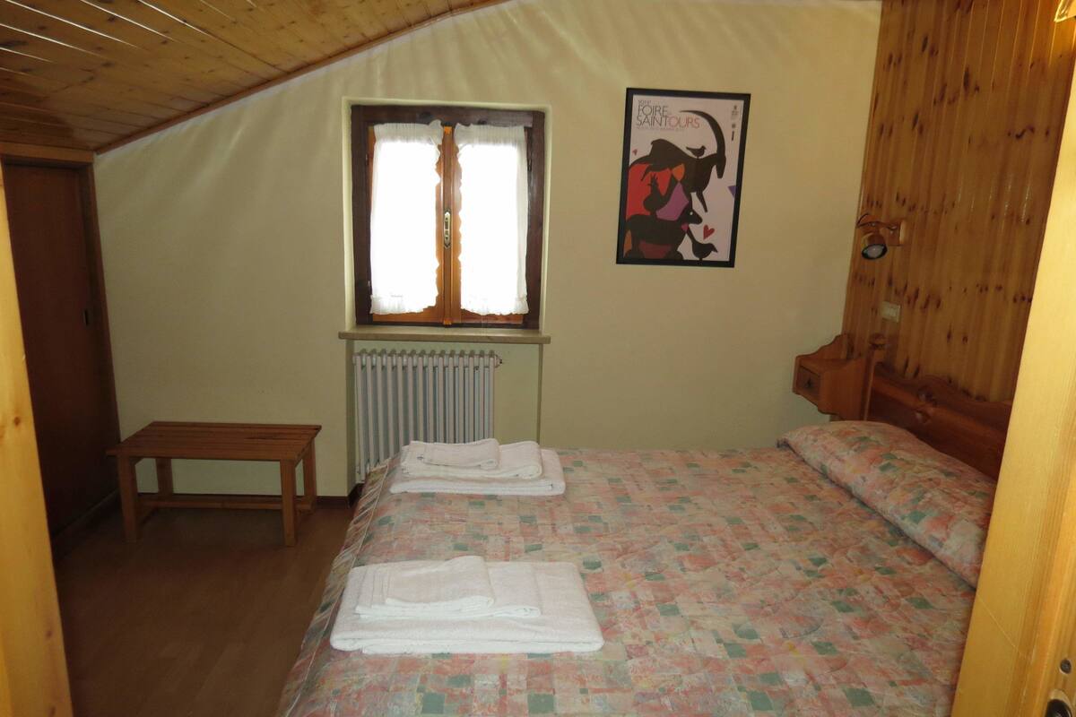 Une chambre à coucher avec un lit, une fenêtre, un radiateur, un banc en bois et une affiche accrochée au mur.