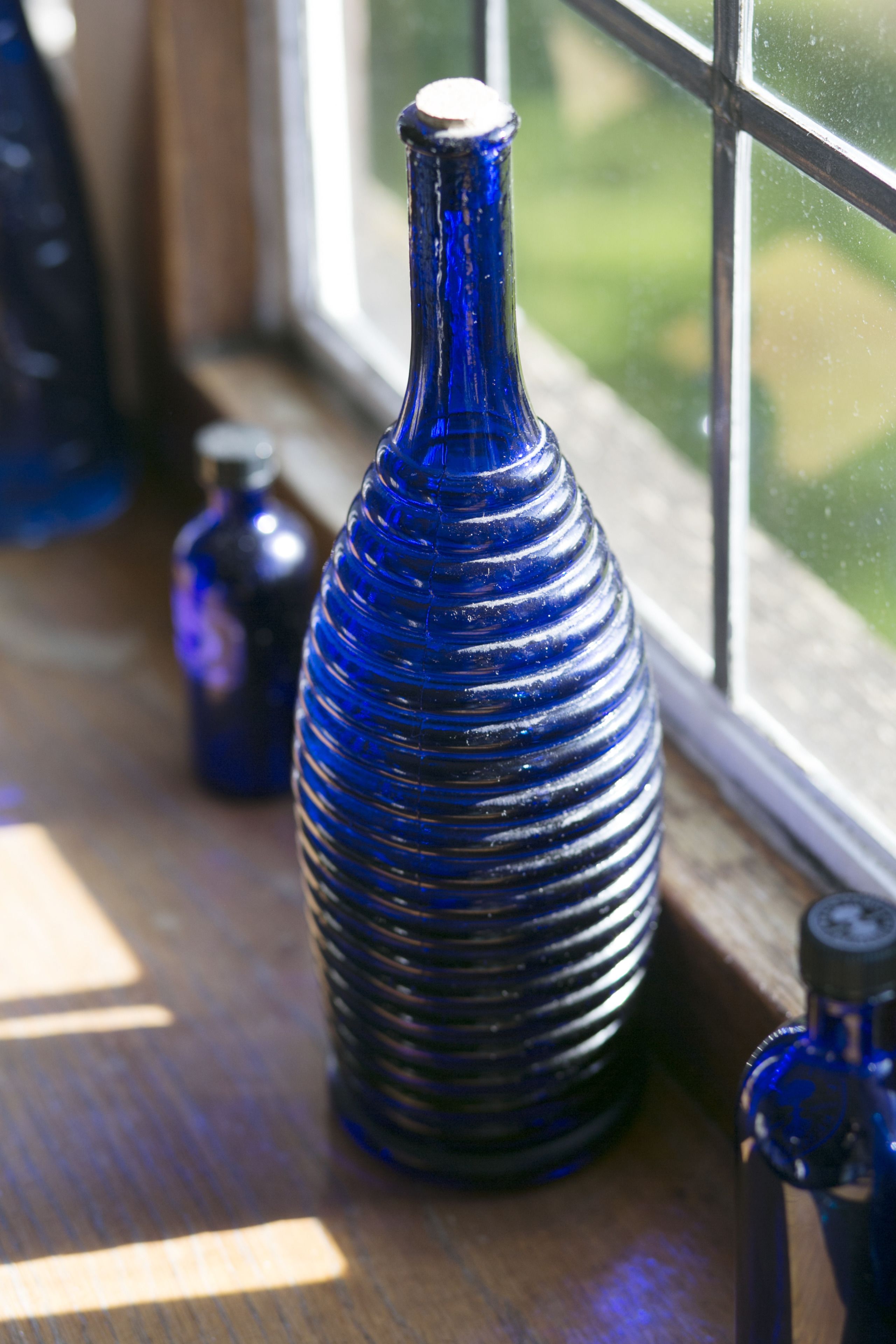 Eine blaue Flasche mit strukturierter Oberfläche auf einem Holzbrett in der Nähe eines Fensters.