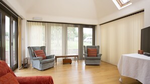 Amplia sala de estar con dos sillones grises, una mesa de centro de madera y una mesa blanca con mantel.