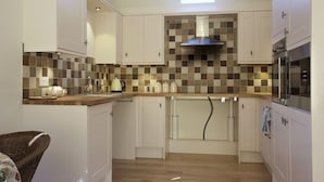 Una cocina compacta con armarios blancos, un salpicadero de azulejos y un horno empotrado.