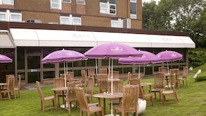 Outdoor wooden tables and chairs arranged in a circular pattern with purple umbrellas. - Premier Inn Carlisle M6 Jct44 (Carlisle)