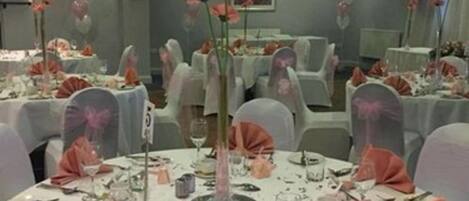 Salão de banquetes com mesas redondas preparadas para um evento formal, com toalhas brancas, guardanapos cor-de-rosa e arranjos florais.
