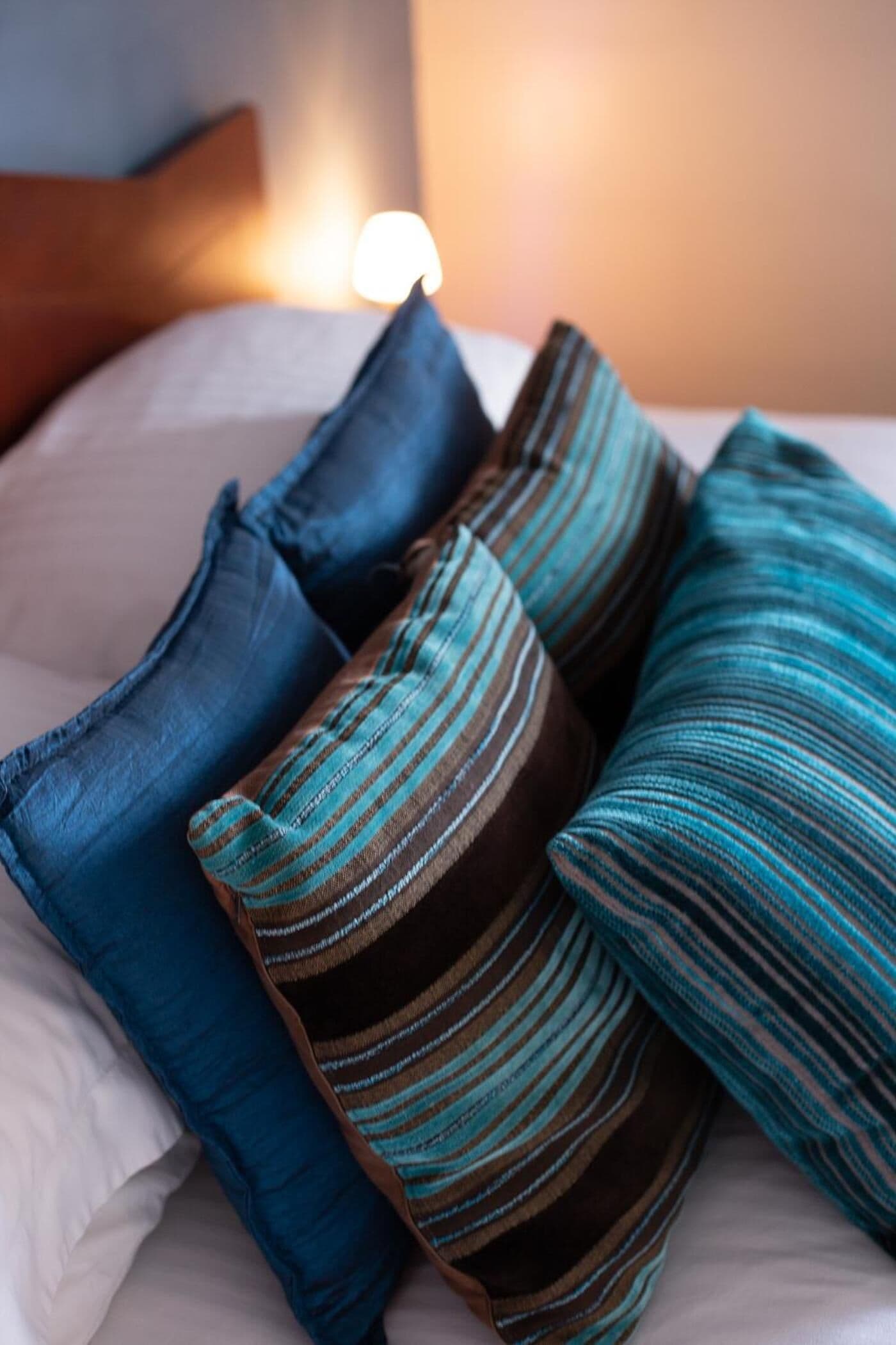 A bed with white sheets and three pillows in shades of blue and brown.