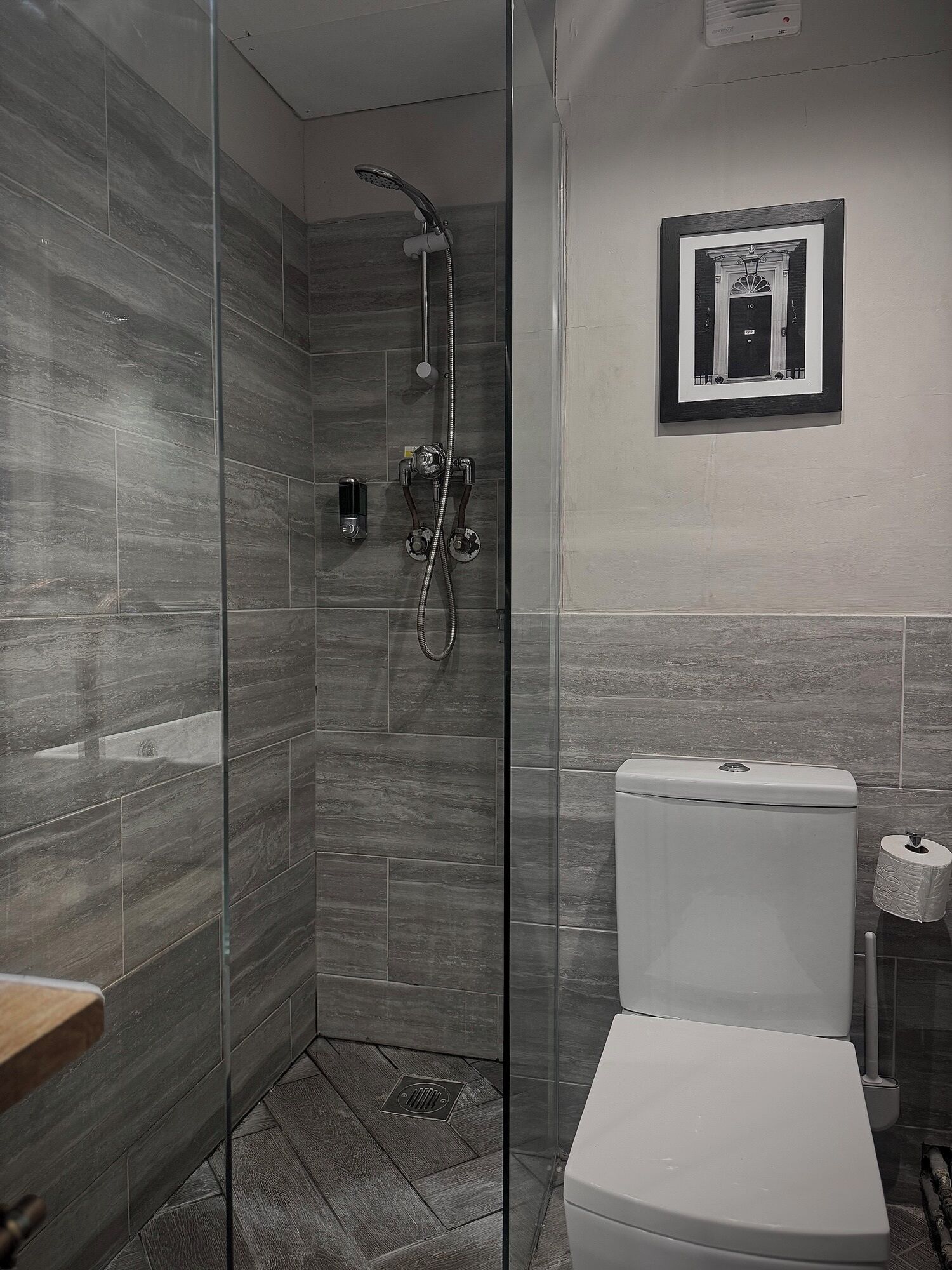 A modern bathroom with a glass-enclosed shower, a toilet, and a framed picture on the wall.