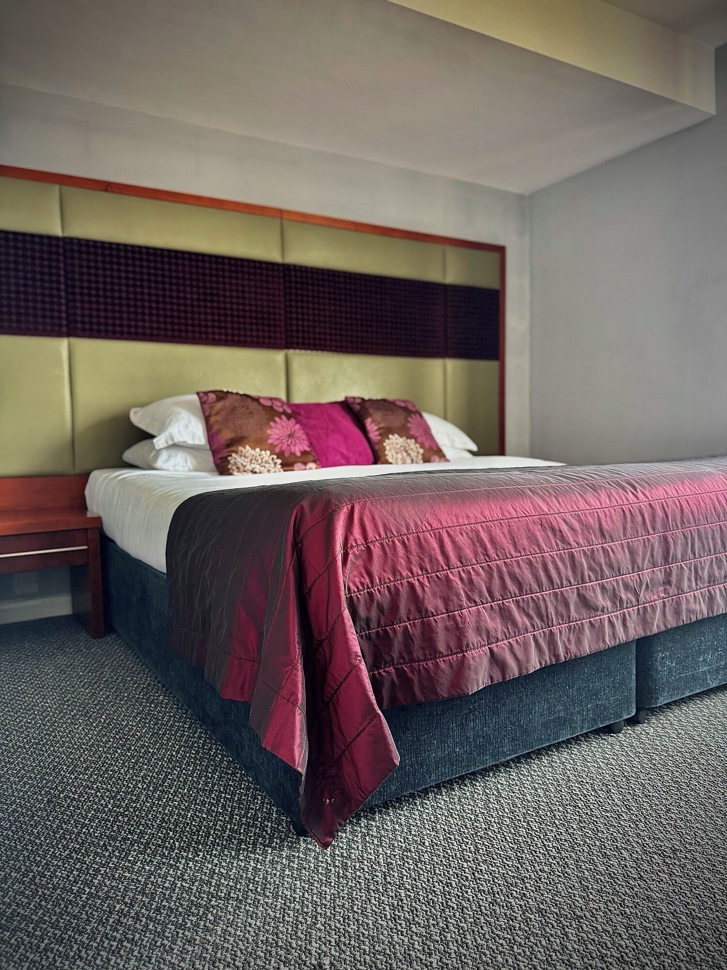 A neatly made bed with a dark blue headboard, a red and black quilt, and white pillows.