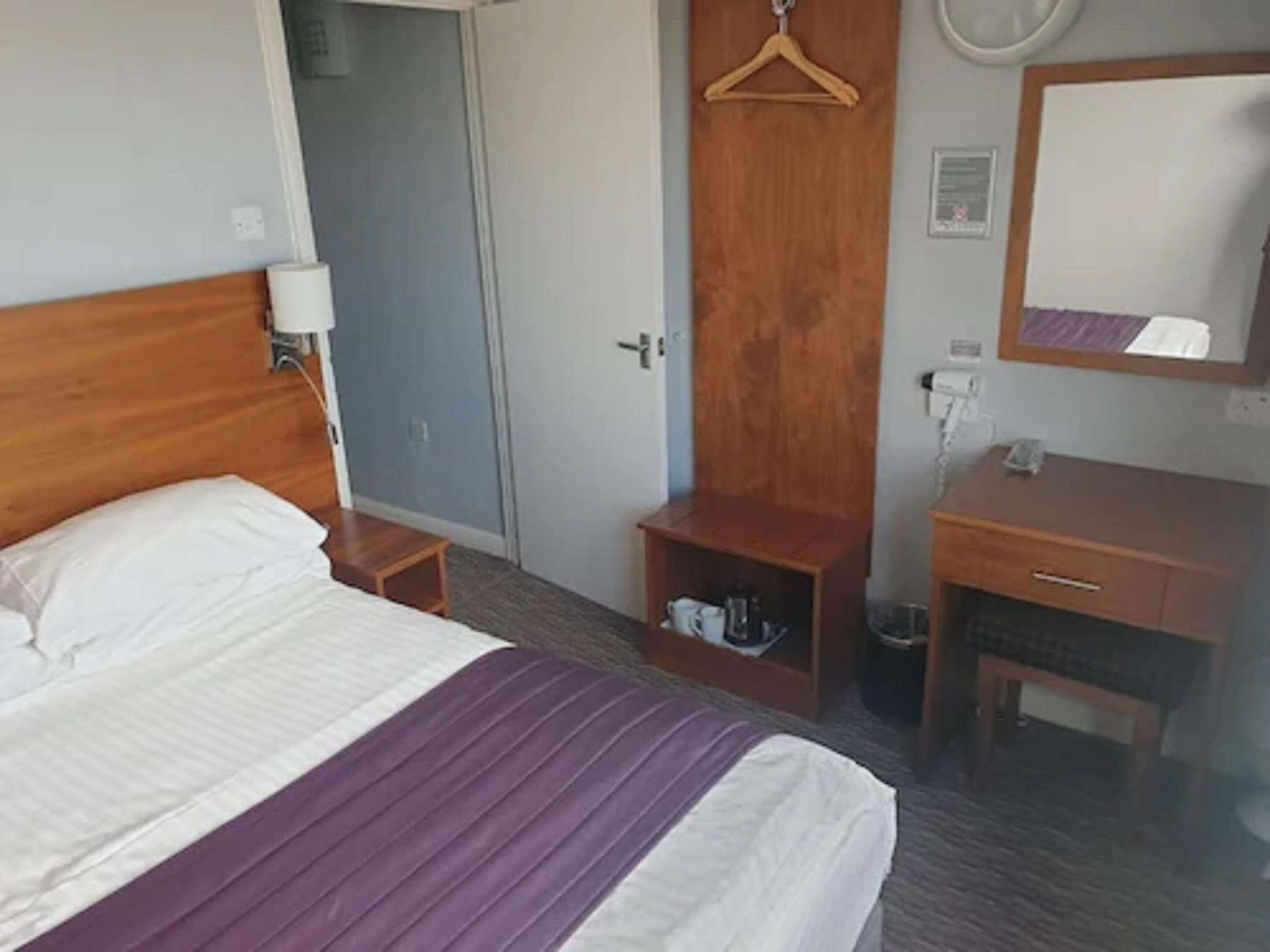 Habitación de hotel con cama, cómoda de madera, espejo y un estante pequeño con artículos de aseo.