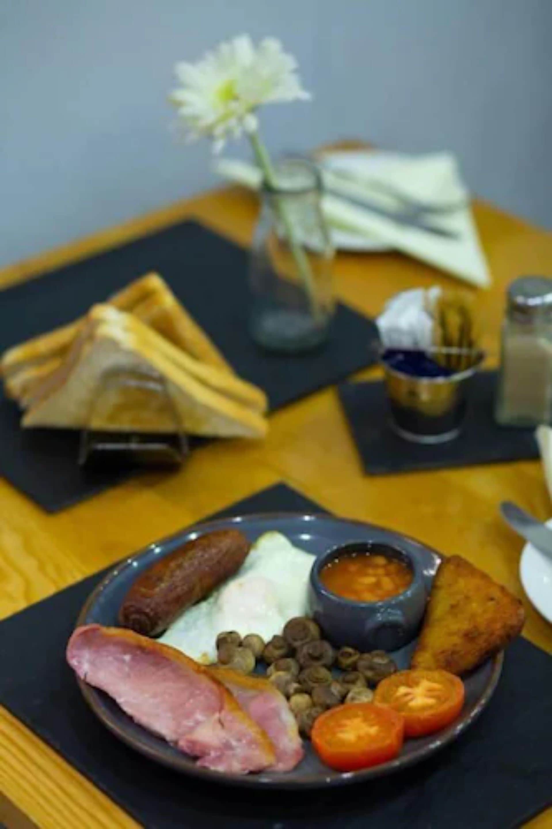 Une assiette de petit-déjeuner comprenant du jambon, des œufs, des saucisses, des tomates et une portion de haricots.