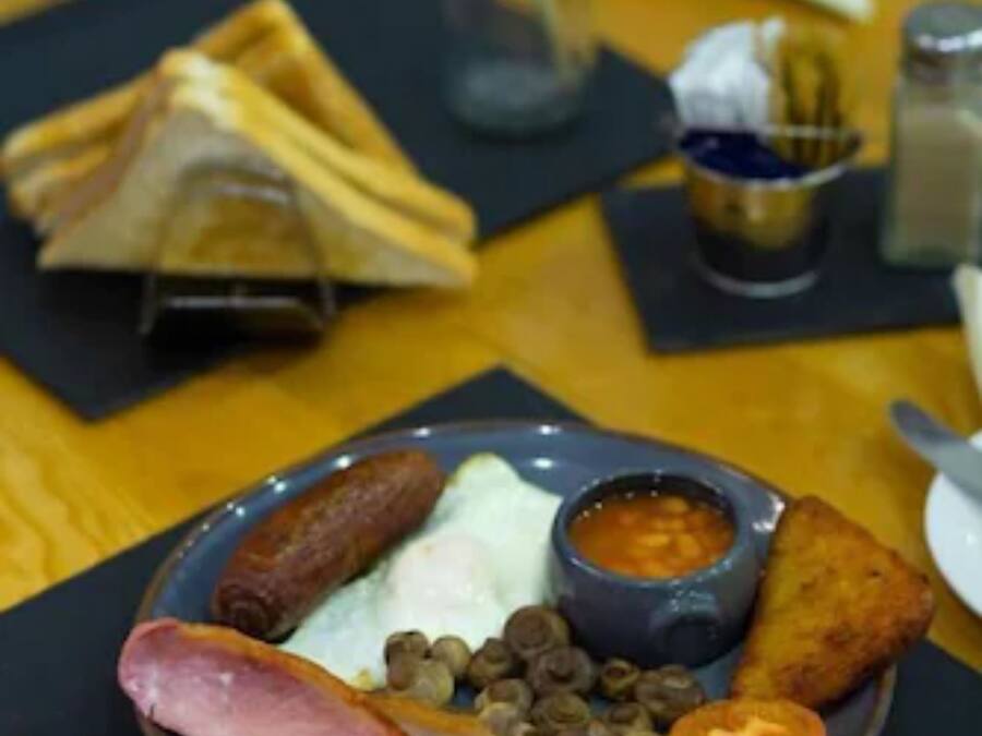 A breakfast plate with ham, eggs, sausages, tomatoes, and a side of beans.