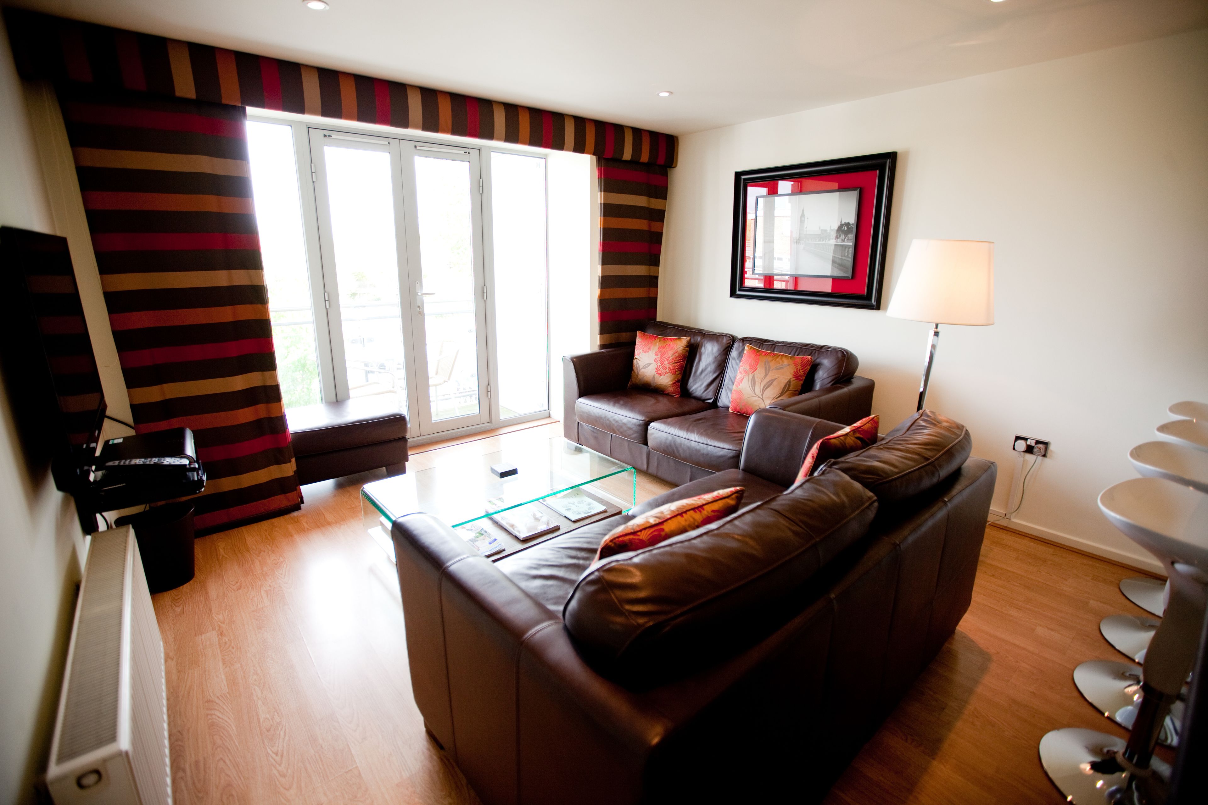 A modern living room with a brown leather sofa, a glass coffee table, and striped curtains.