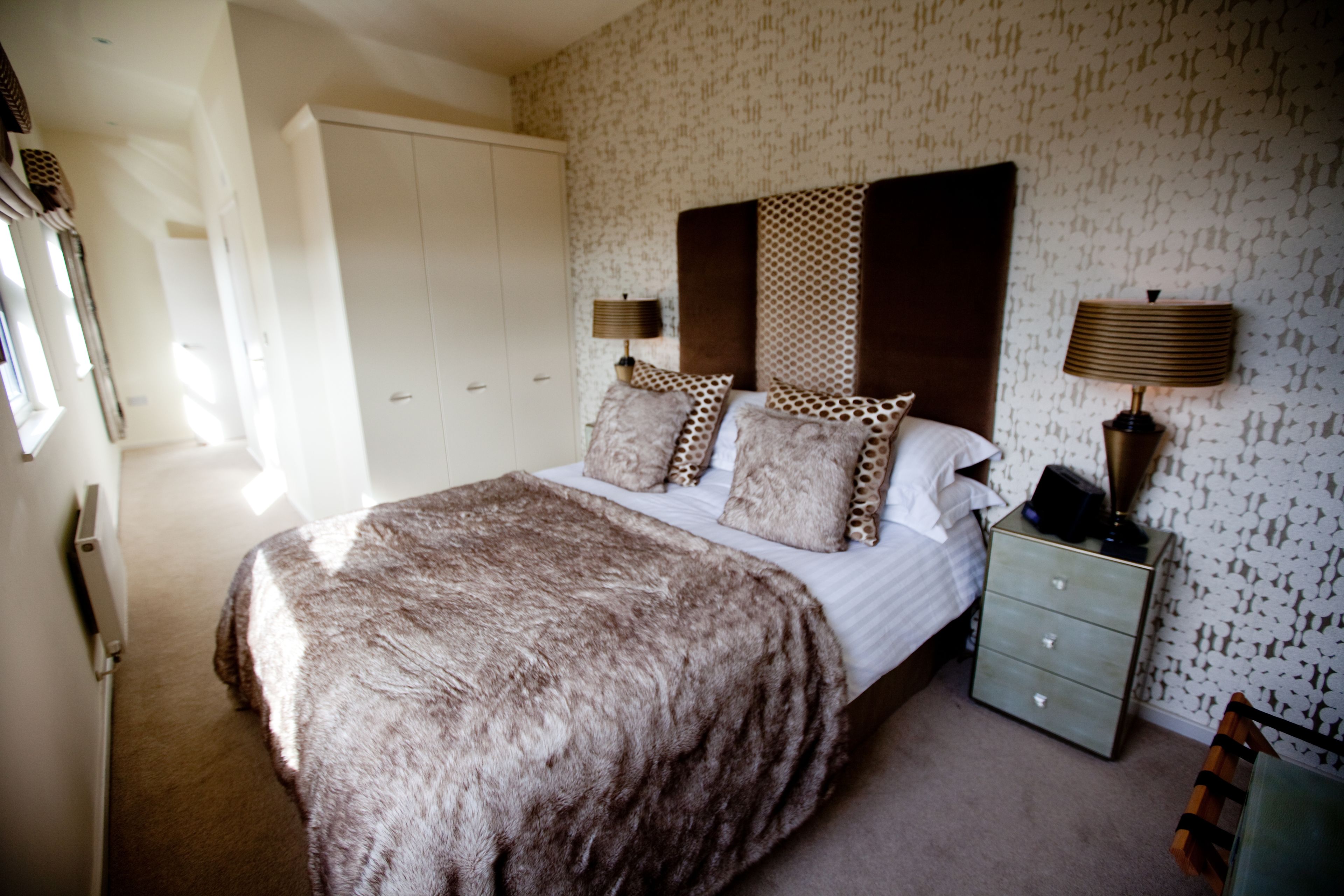A bedroom with a large bed, two bedside tables with lamps, a wardrobe, and patterned wallpaper.