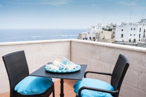 Ein Balkon mit Korbstühlen und einem Tisch mit Blick auf eine Küstenstadt.
