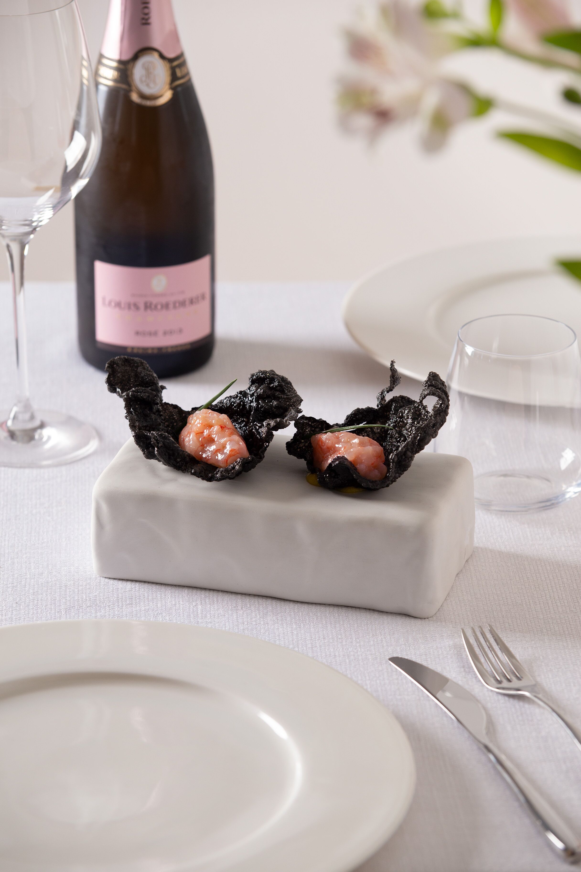 En desserttallerken med en rosevinflaske og et vinglas på et bord.