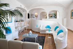 A spacious living area with white furniture, a glass coffee table, and a large plant.