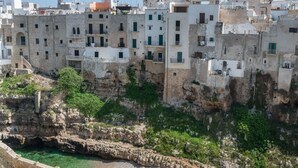 A coastal town with historic stone buildings, a prominent tower, and a rocky shoreline. - Covo dei Saraceni (Polignano a Mare)