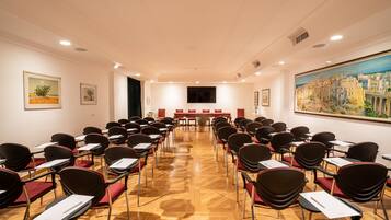 Un salón de conferencias con filas de sillas, un cuadro grande en la pared y una pantalla de televisión al frente.