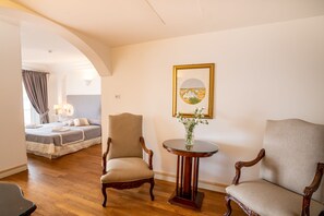 Ein Hotelzimmer mit einem Bett, zwei Sesseln, einem runden Tisch mit einer Vase und einem gerahmten Bild an der Wand.