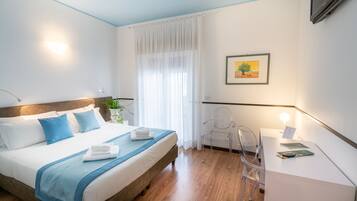 Una camera d'albergo moderna con un letto rifatto, una scrivania con una lampada e un'ampia finestra con tende leggere.