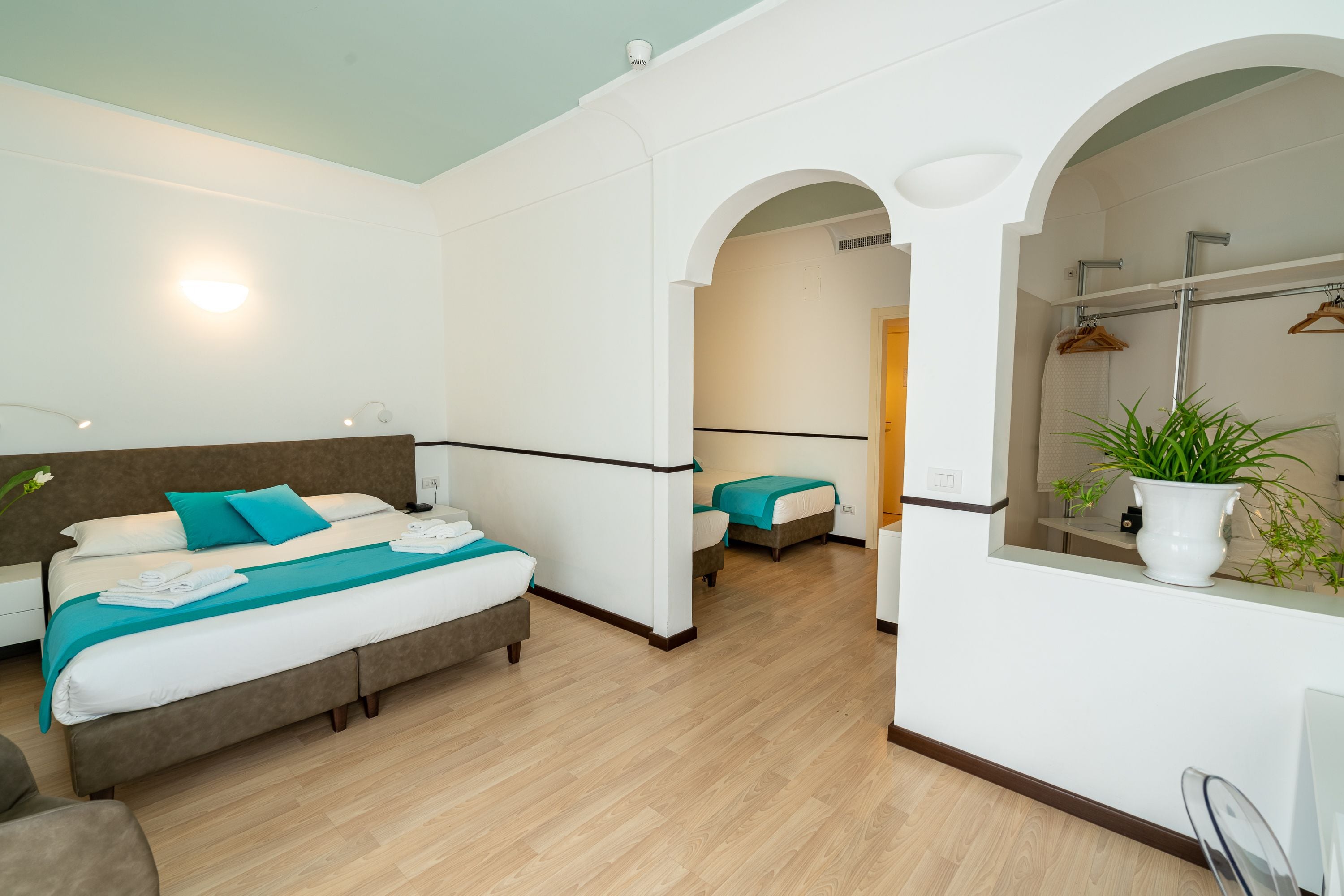 Une chambre d’hôtel moderne dotée d’un grand lit, d’un lit plus petit et d’un coin salon. La salle de bain est équipée d’une douche et d’un miroir.