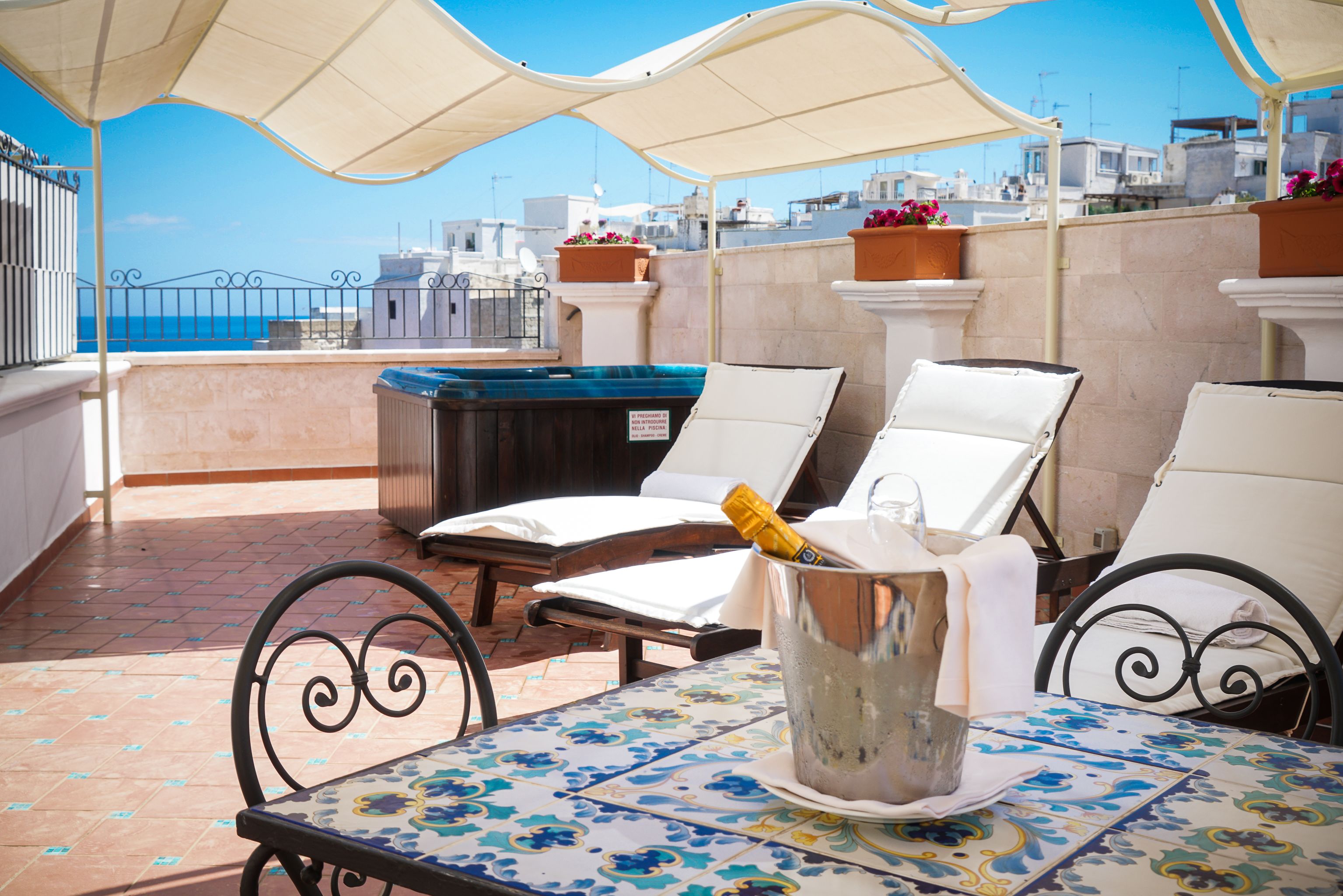 Una terraza con dos tumbonas, una mesa con una botella de champán y vistas al mar y a los edificios.
