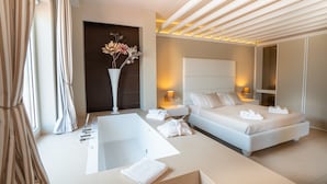 A modern hotel room with a large bathtub, a bed with white linens, and a vase of flowers on the wall. - Covo dei Saraceni (Polignano a Mare)