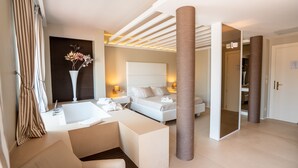 A modern hotel room with a large bed, a sitting area with a sofa and a small table, a bathtub, and a large mirror. - Covo dei Saraceni (Polignano a Mare)