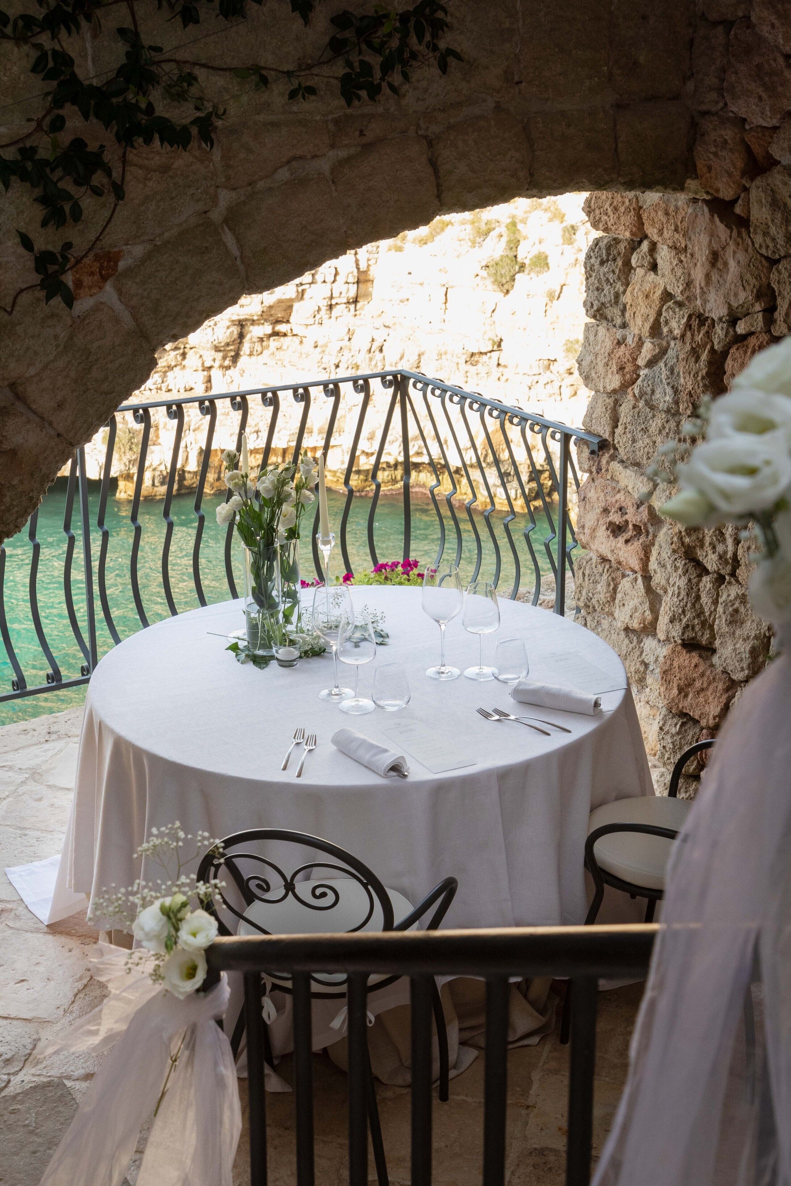 A round table set for a meal with a view of a rocky cliff and water.