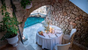 A table set for two with candles, a potted plant, and a stone wall backdrop. - Covo dei Saraceni (Polignano a Mare)