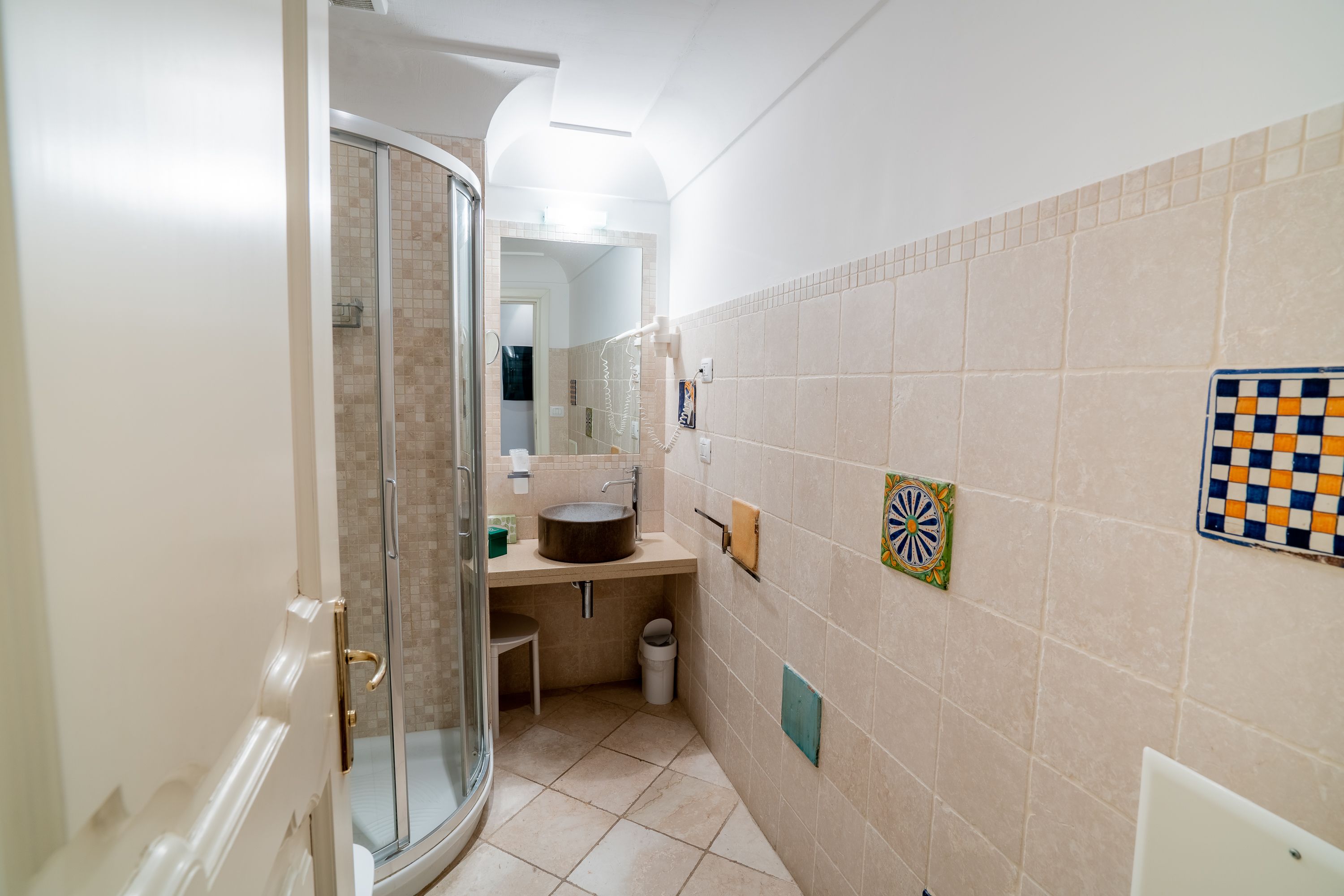 A bathroom with a glass shower enclosure, a sink with a round basin, and tiled walls with decorative tiles.