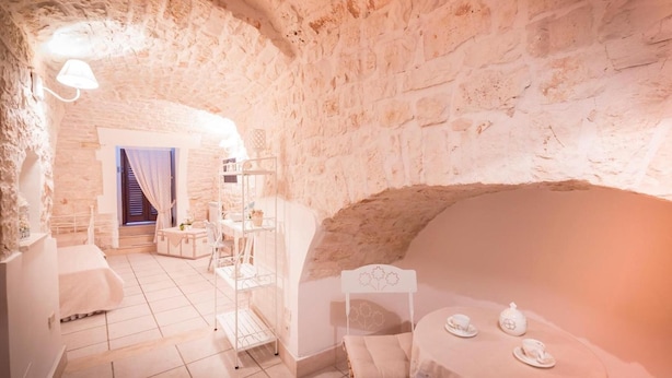 A cozy room with a stone wall, a bed, a table with tea set, and a chair.