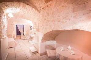 A cozy room with a stone wall, a bed, a table with tea set, and a chair. - Relais del Marchese (Turi)