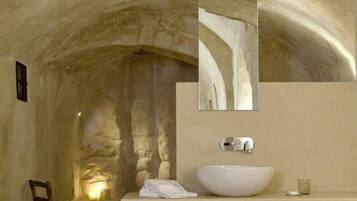 Un baño con techo abovedado de piedra, un lavabo grande de color blanco y un espejo encima.