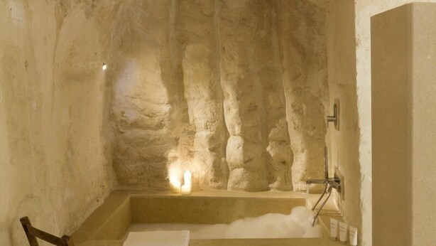 A stone-walled bathroom with a bathtub, a wooden chair, and a towel rack. - Corte San Pietro (Matera)