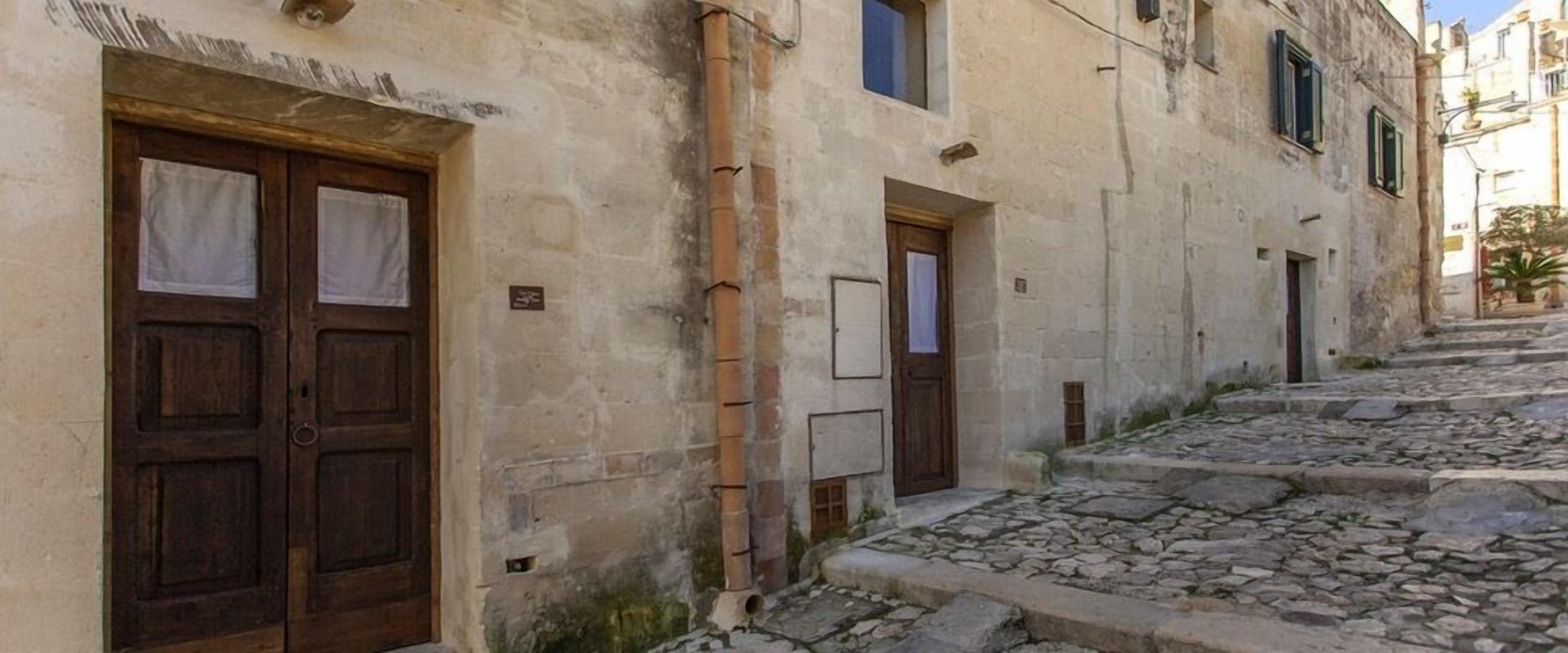 A narrow stone-paved street with traditional buildings, wooden doors, and a rustic appearance.