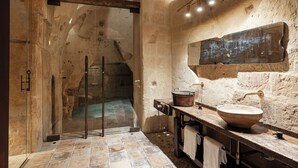 A rustic bathroom with a stone wall, a wooden sink, and a glass shower enclosure. - Corte San Pietro (Matera)