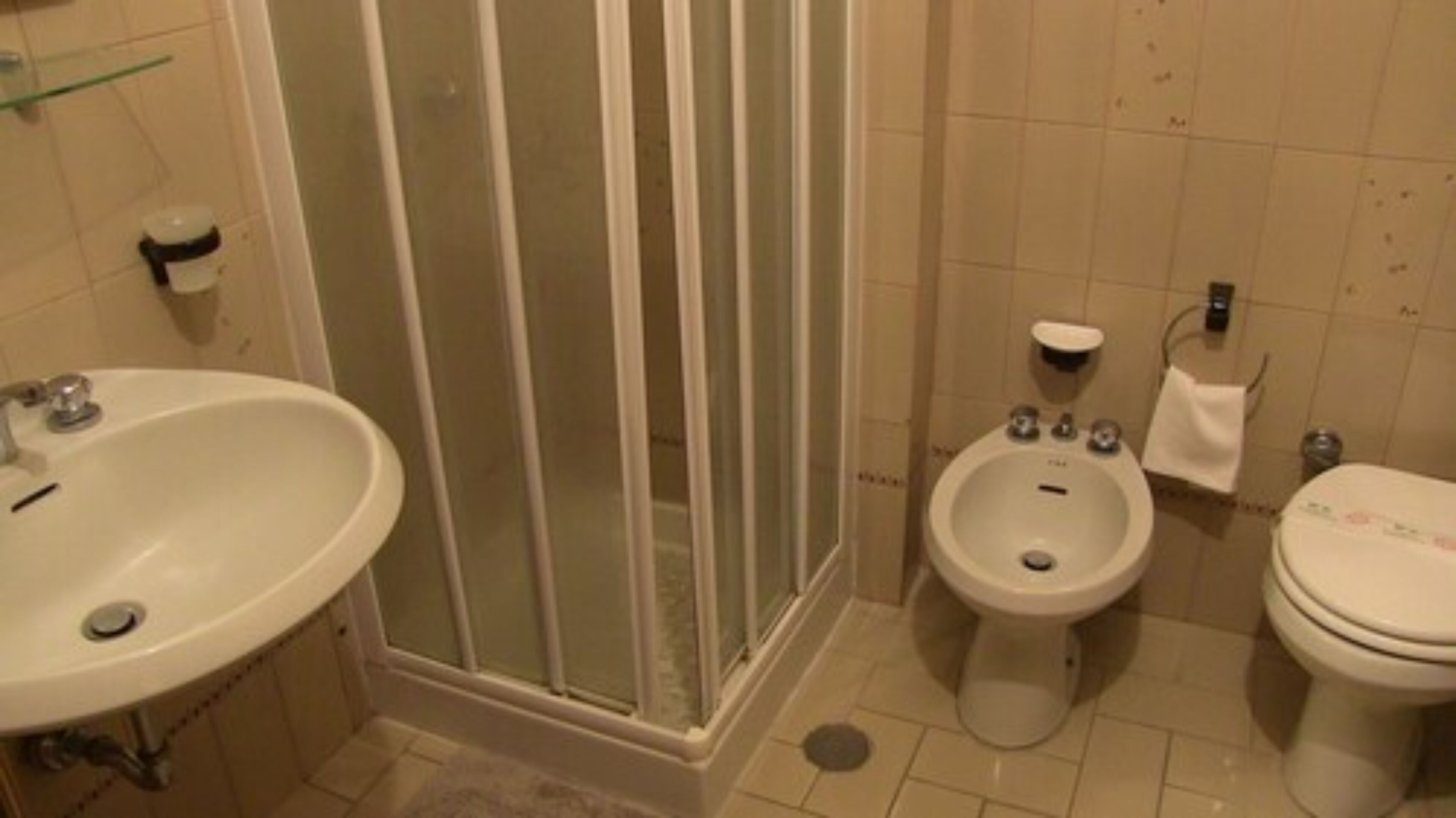A bathroom with a sink, bidet, toilet, and a glass-enclosed shower.