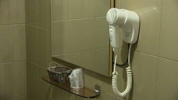 A hairdryer mounted on a wall in a bathroom with a basket and a plastic container on a shelf.