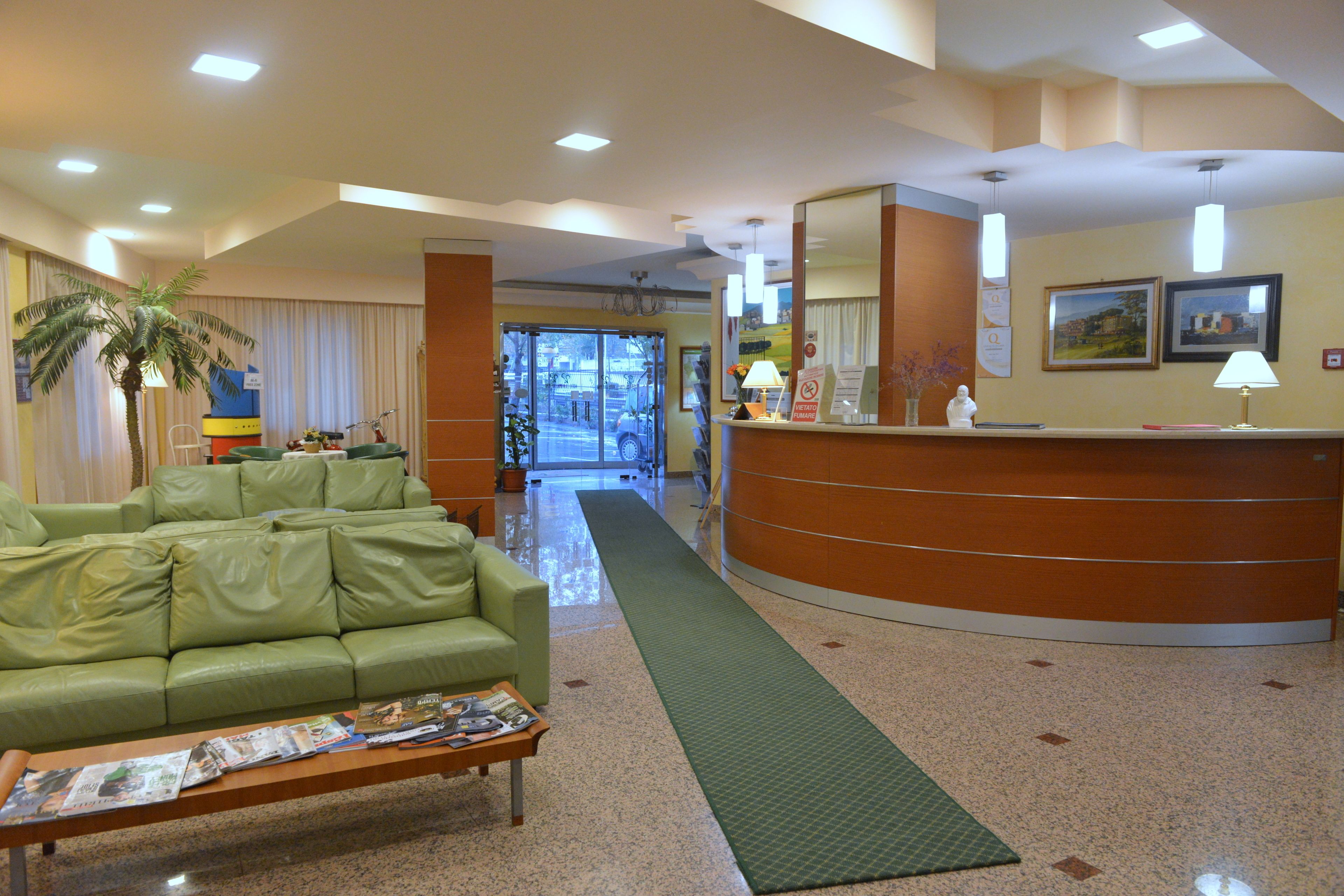 A reception area with a green sofa, a reception desk, a mirror, and a green mat leading to the entrance.