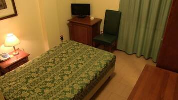A hotel room with a bed, a desk with a lamp, a chair, a television, and a curtain.