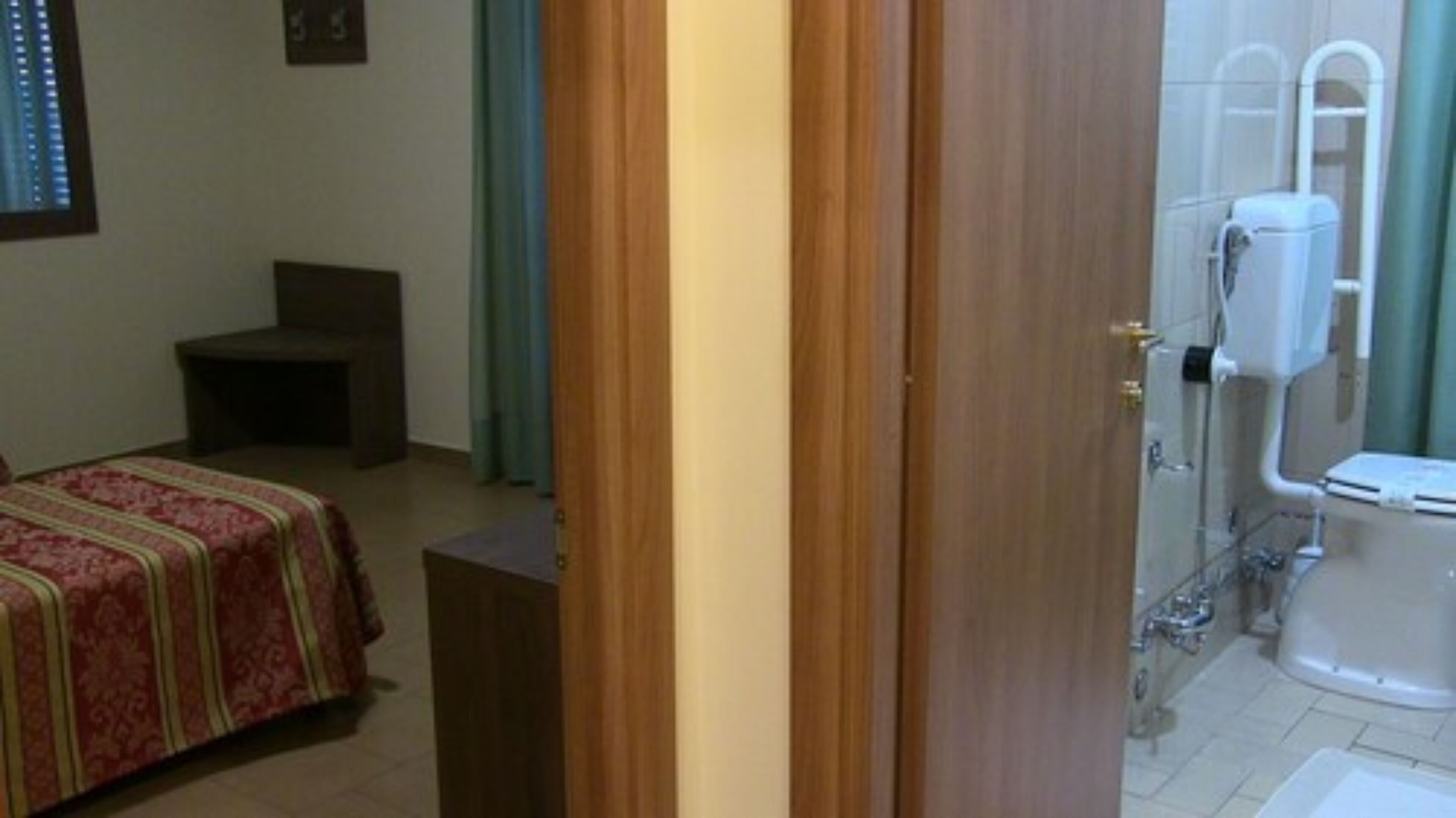 Una camera da letto con un letto, un comodino e uno sgabello. È presente un bagno con il water, una doccia e un lavandino.