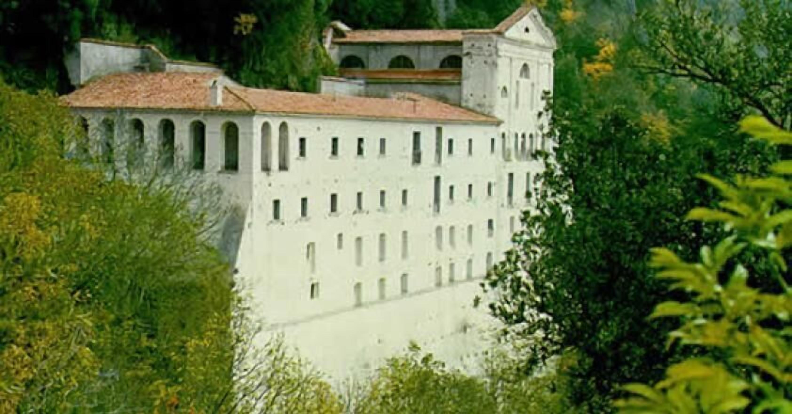 A large, white building with multiple windows and a tower, surrounded by lush greenery.