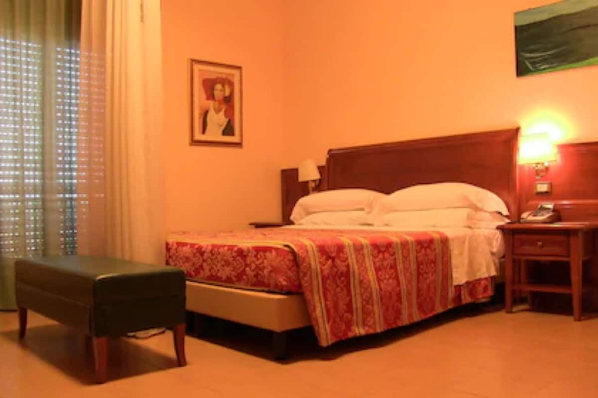 Una habitación de hotel con cama, mesita de noche, lámpara y un banco.