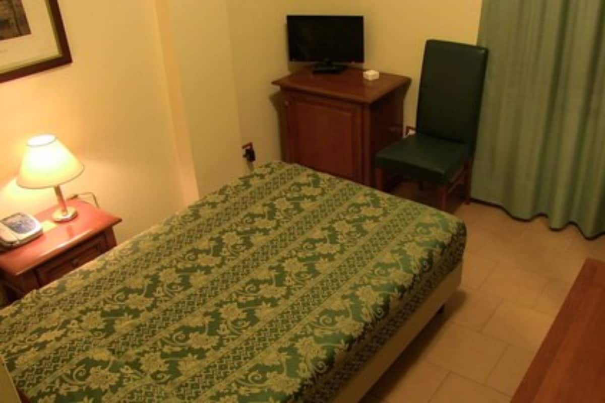 Una habitación de hotel con cama, escritorio con lámpara, silla y televisión.