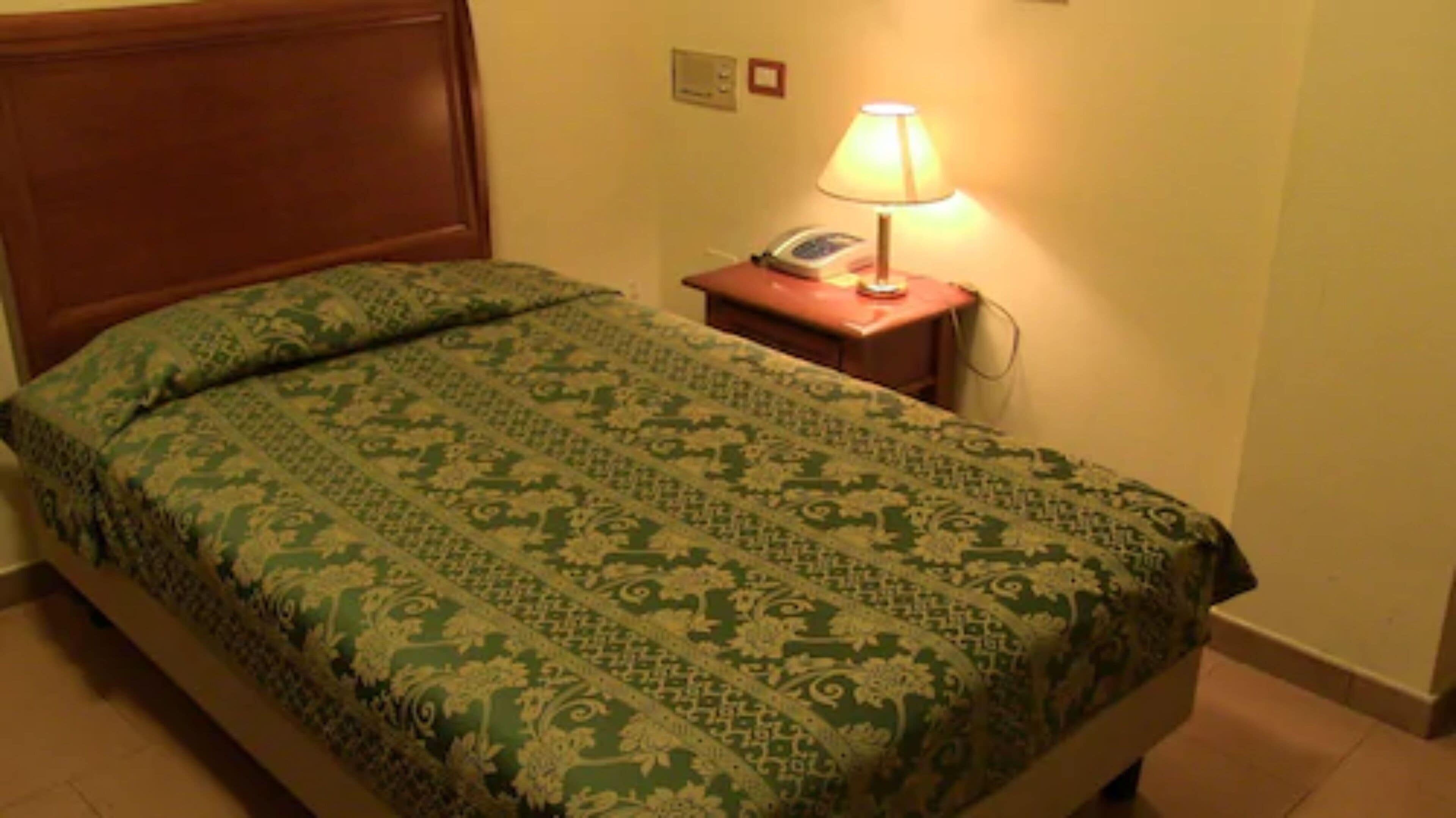 A hotel room with a bed, a nightstand, a lamp, and a telephone.