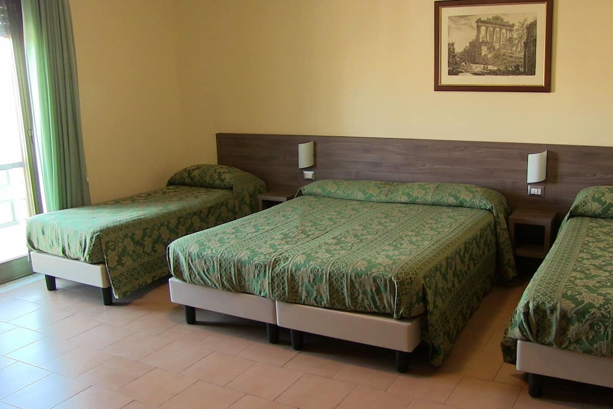 Habitación de hotel con tres camas individuales, cabecera de madera, un cuadro en la pared y una ventana con cortinas.